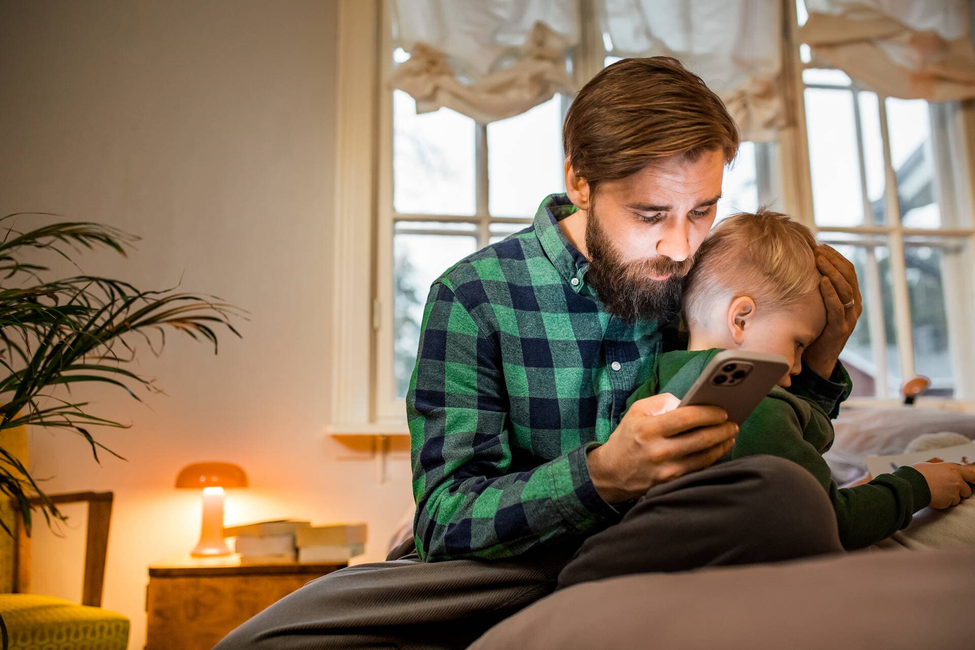 Isä pitää sairasta lasta sylissään ja käyttää Digiklinikkaa puhelimellaan.