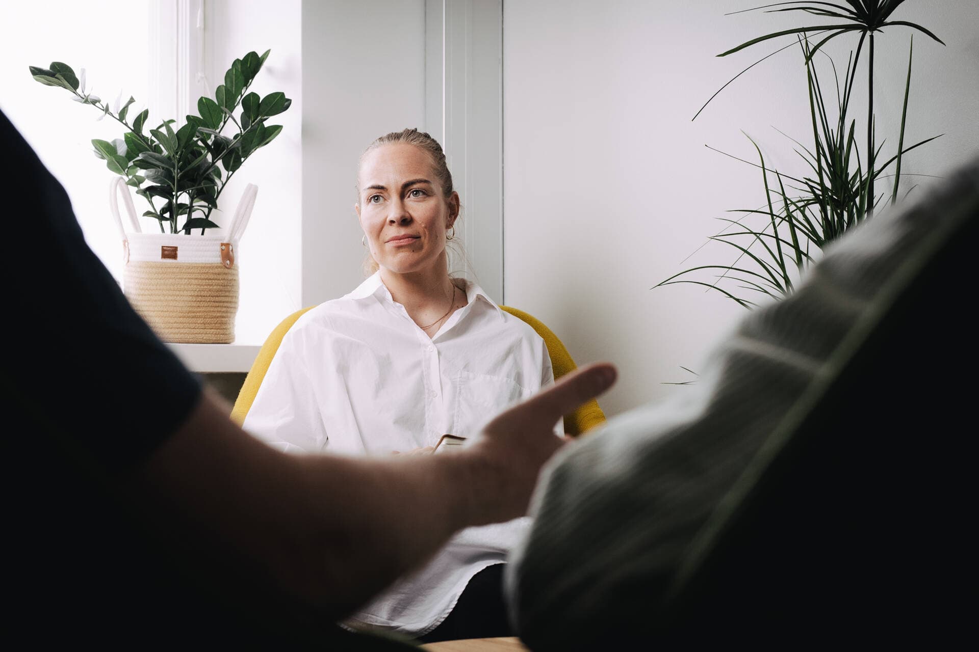 Neuropsykologi istuu hymyillen vastaanottotuolillaan katsoen asiakasta.