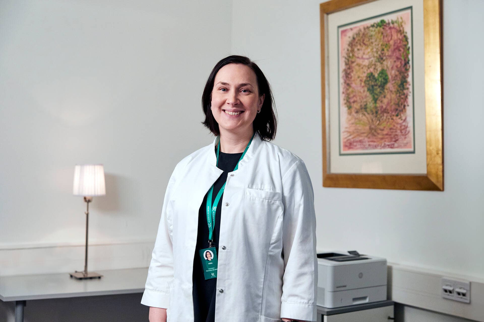 Mehiläinen’s gynaecologist smiles and stands in front of a colourful painting.