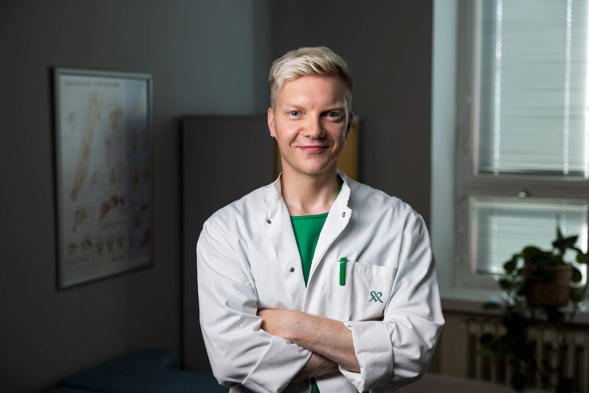 Mieslääkäri poseeraa kameraan hymyillen hämärässä vastaanottohuoneessa.
