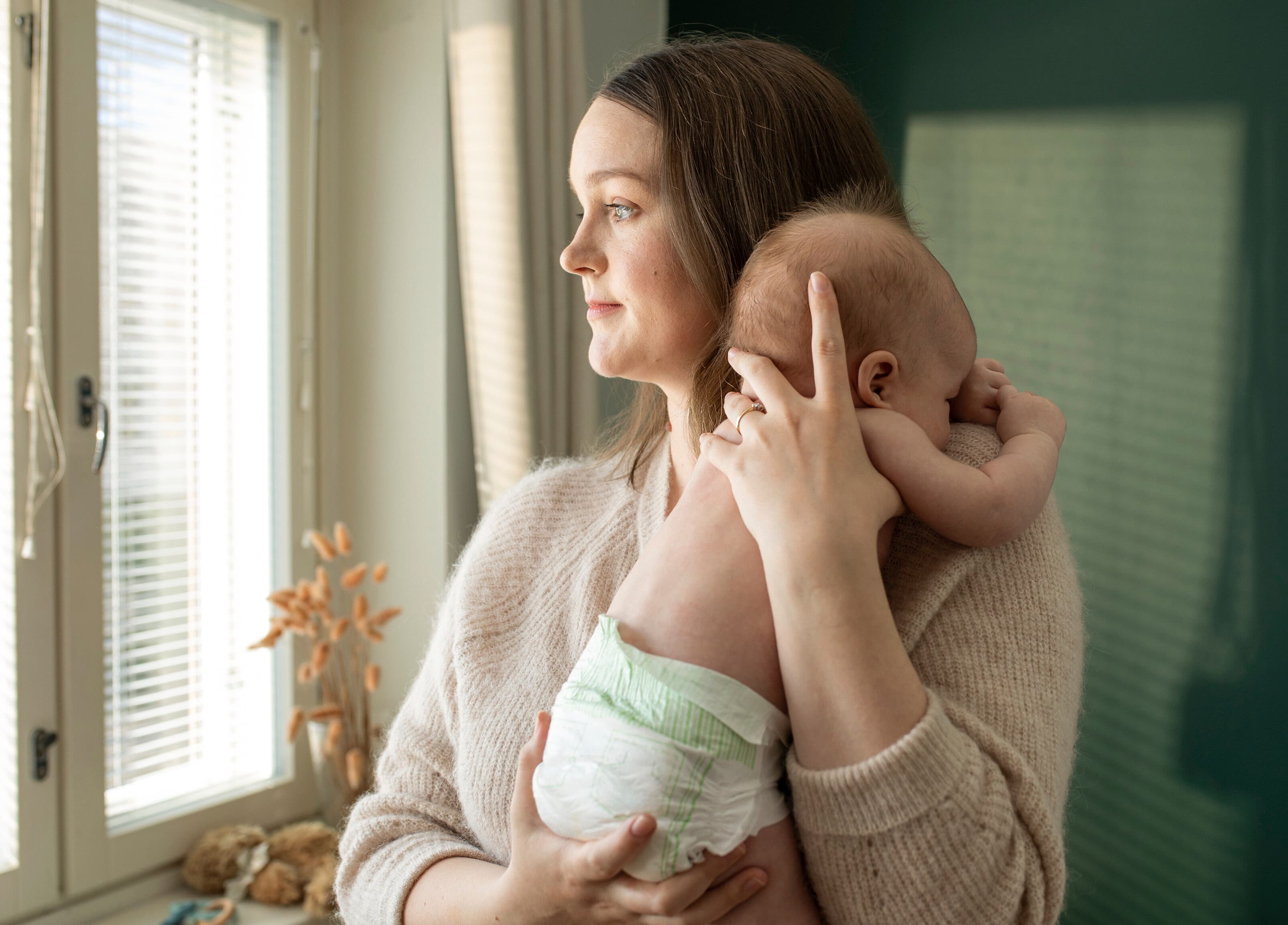 A woman is holding a baby in her arms and looking out the window.