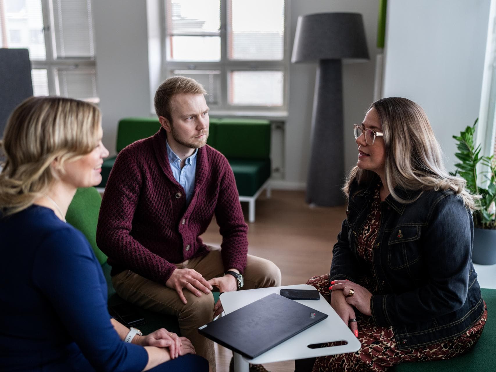 Kaksi naista ja mies istuvat sisällä ja keskustelevat