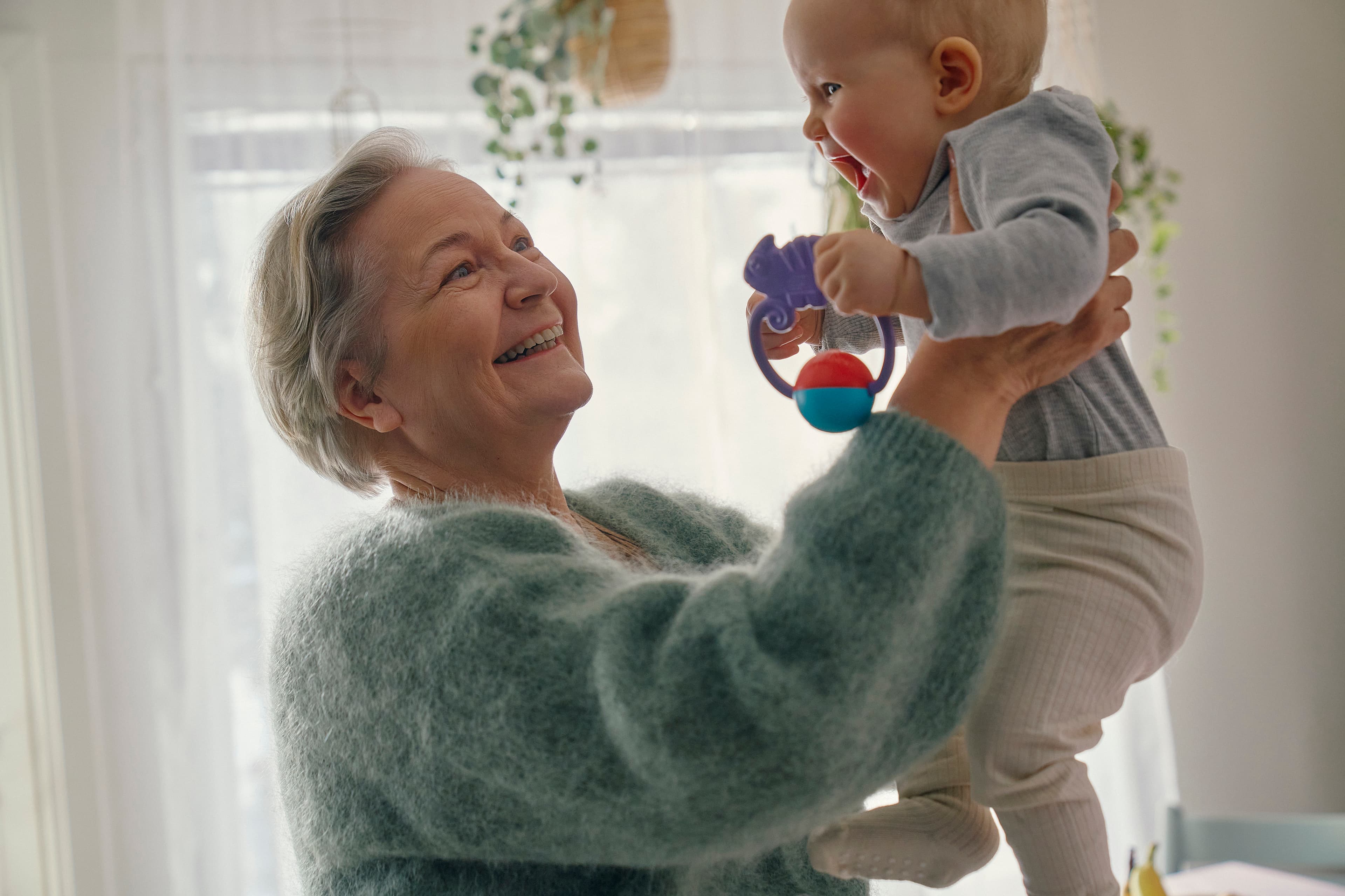 An older woman lifts a baby into the air and smiles.