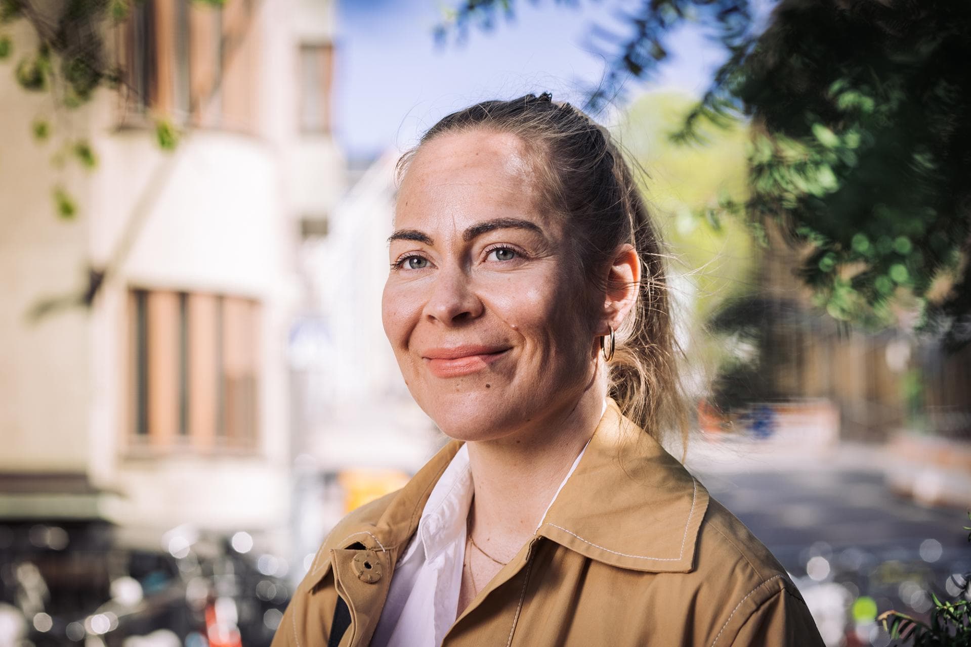 Nainen hymyilee iloisesti kauniina kesäpäivänä puistossa ilman silmälaseja.