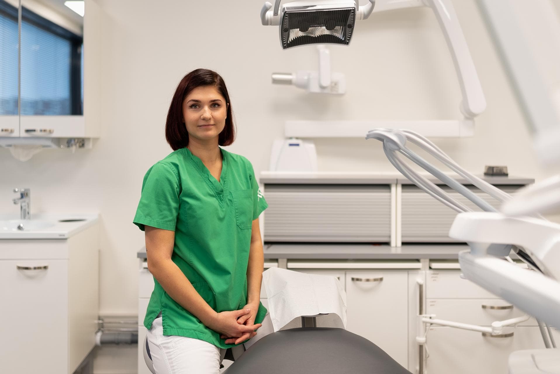 A dental nurse sits in the treatment room and looks at the camera.