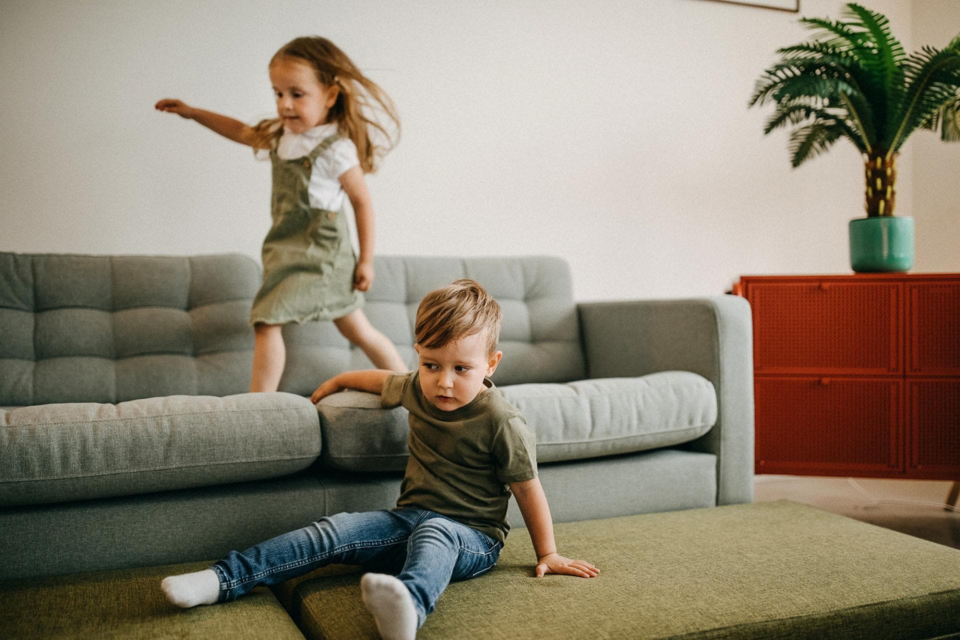 Ylivilkas lapsi hyppii sohvalla ja toinen lapsi istuu lattialla.