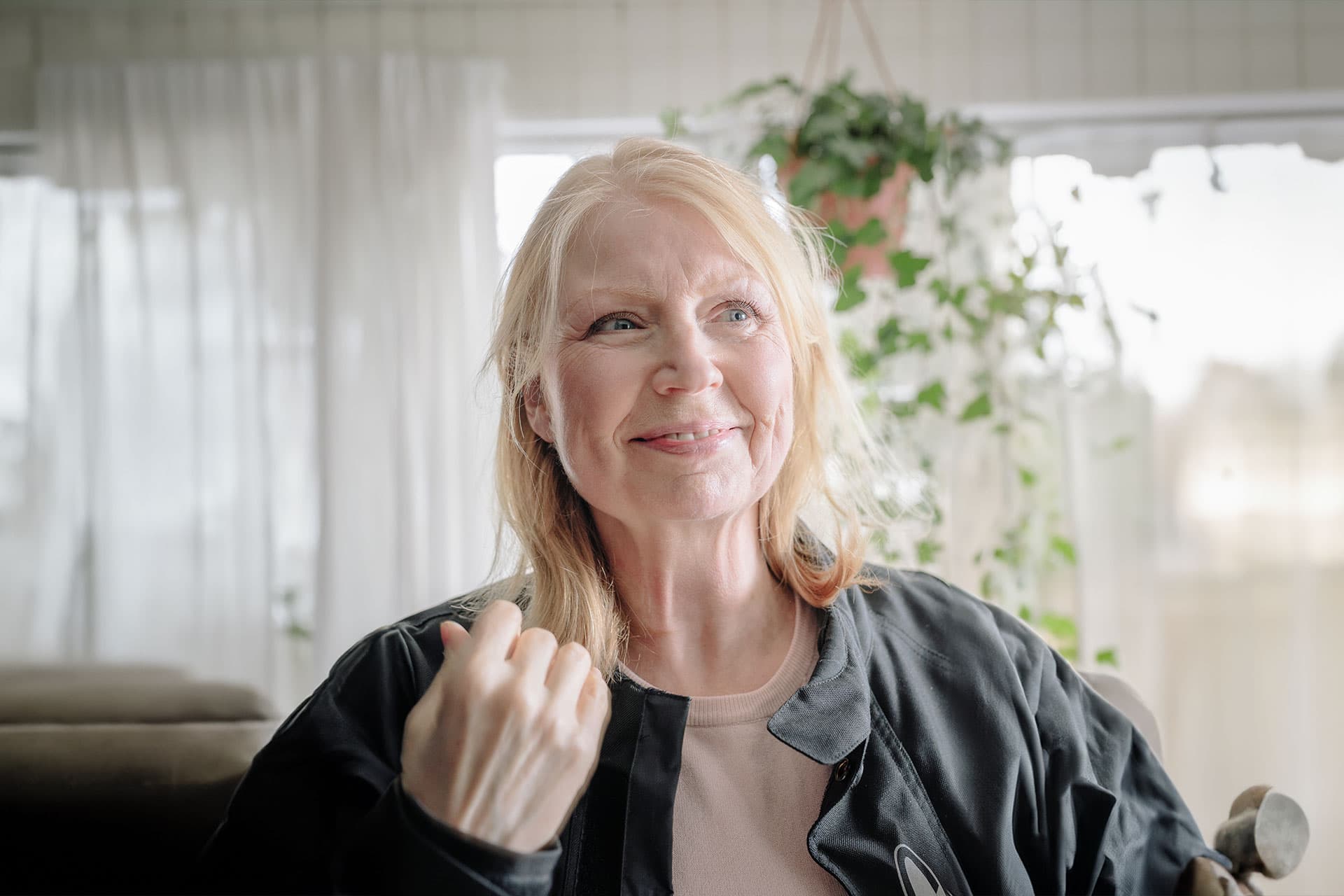 Iäkkäämpi vaaleahiuksinen nainen hymyilee tyytyväisenä.