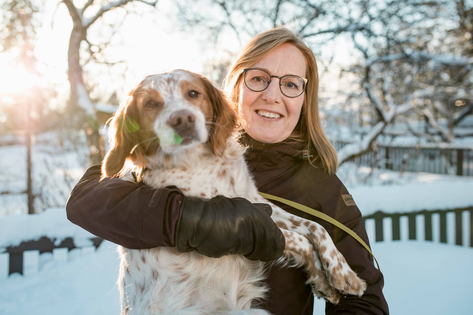 Nainen pitää hymyillen koiraa sylissään ulkona talvella.