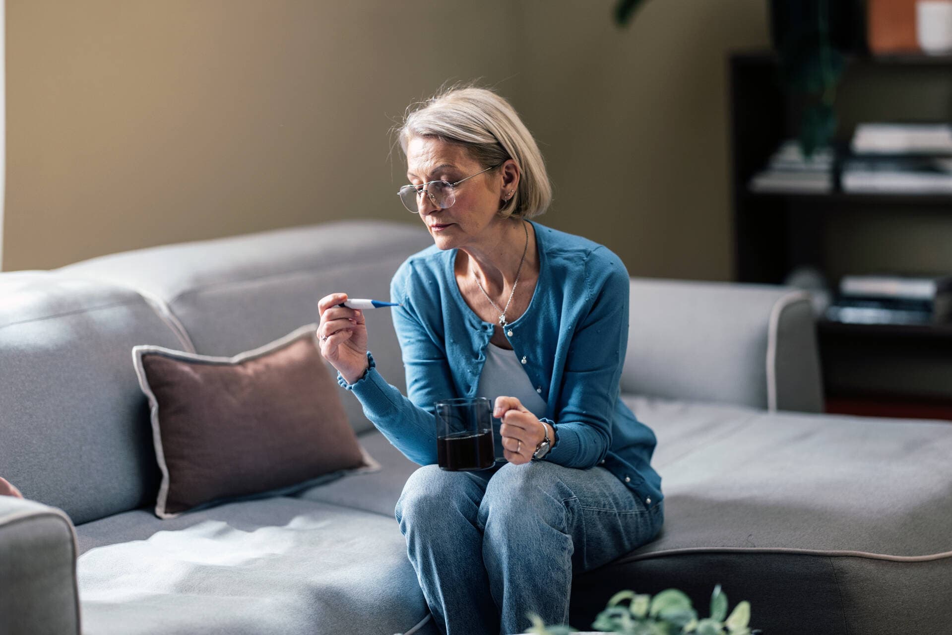 A person sitting on a sofa and looking at a thermometer.