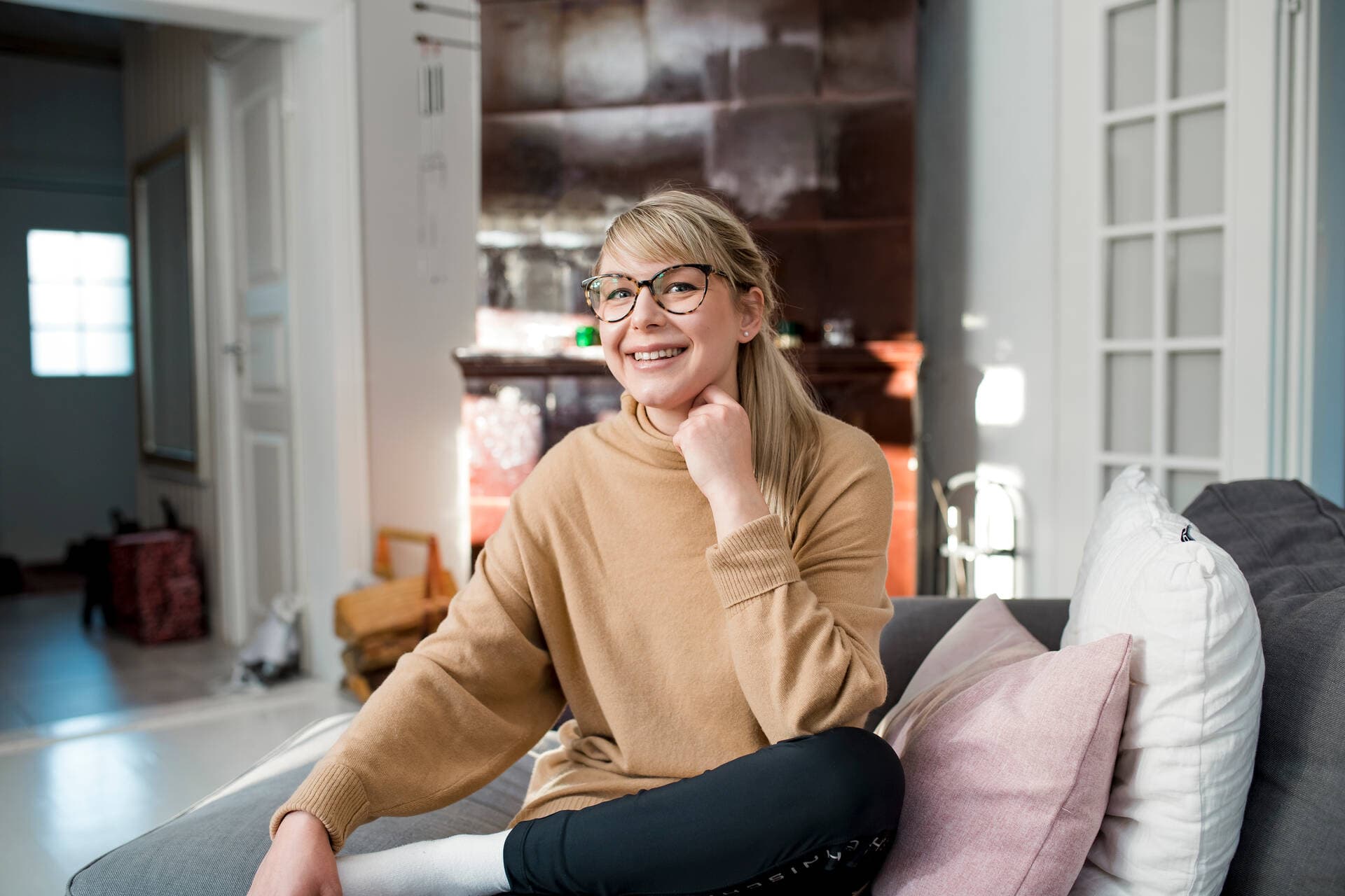 Mielenterveyden ammattilainen istuu sohvalla ja katsoo kameraan hymyillen.