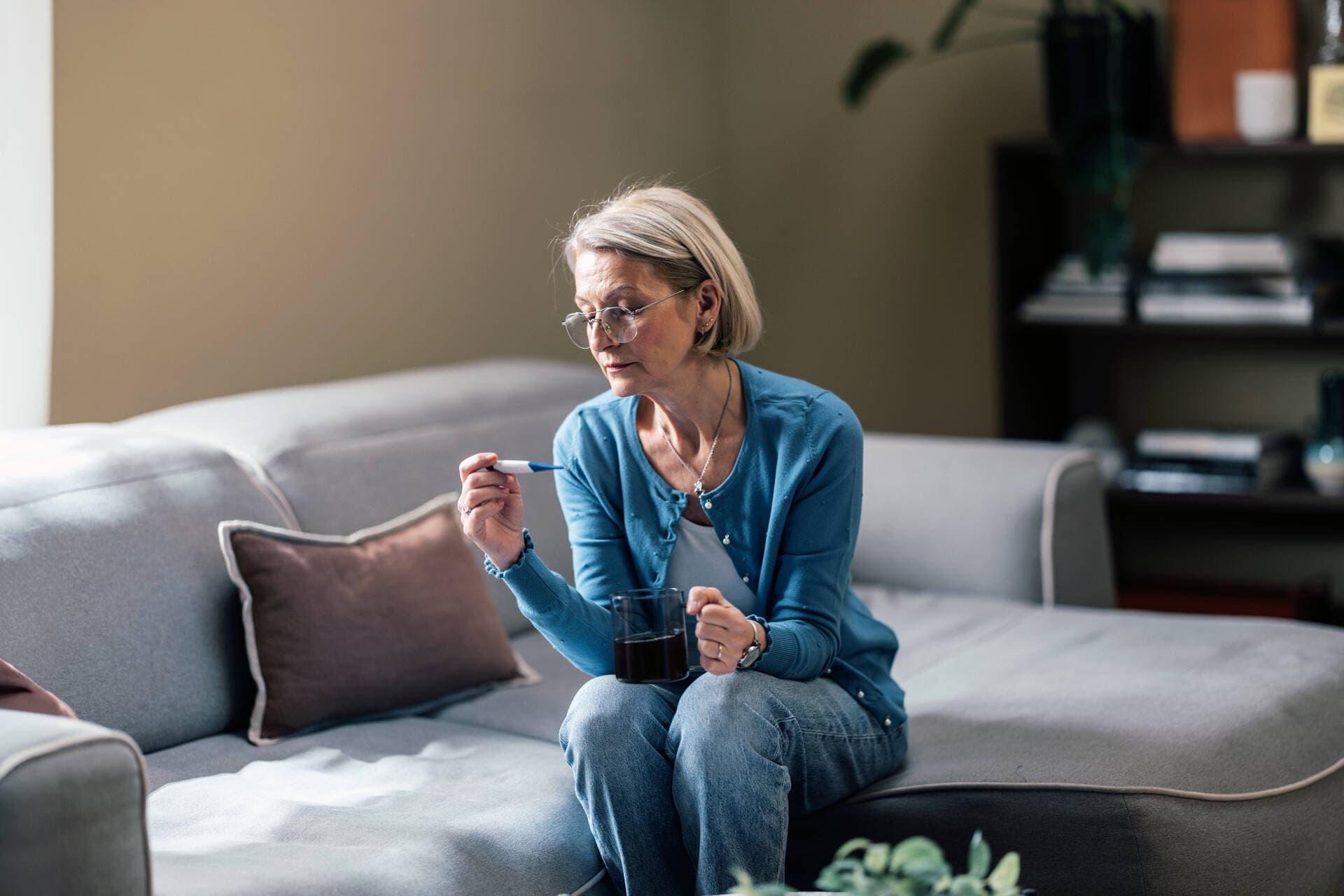 En person sitter i en soffa och tittar på en febertermometer i sin hand.