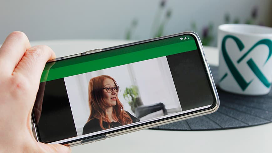 Asiakas pitää puhelinta kädessään ja katsoo OmaMehiläisen Videokirjaston videota.