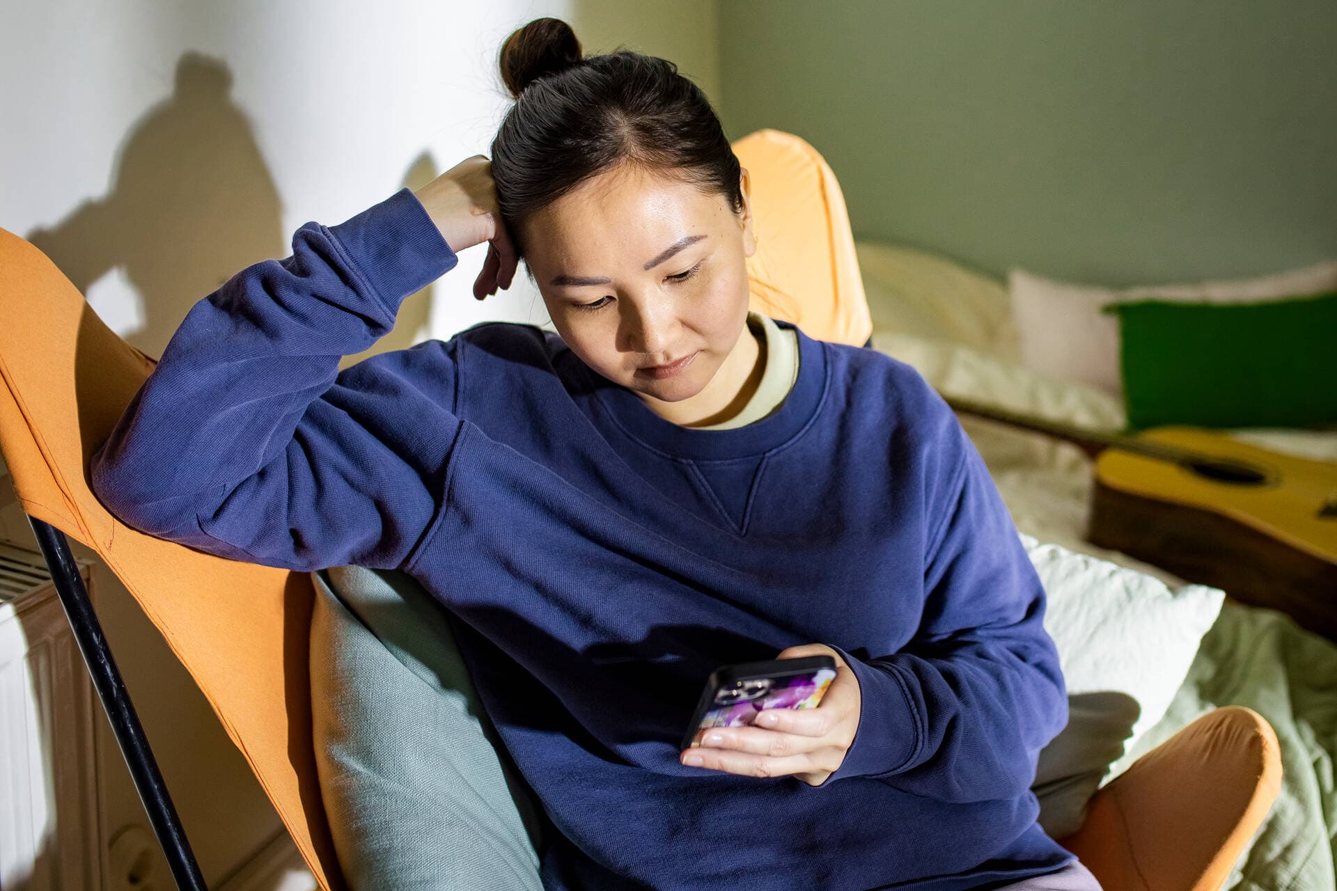 En person sitter i en fåtölj med en telefon i sin hand.
