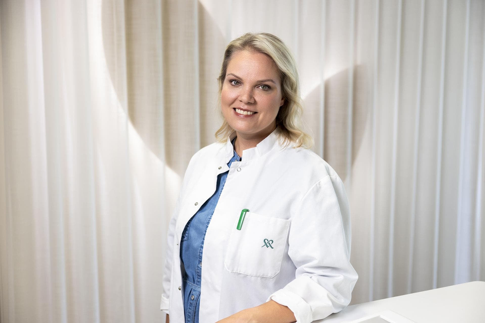 Mehiläisen lääkäritakkiin pukeutunut lääkäri Hanne hymyilee kameralle.