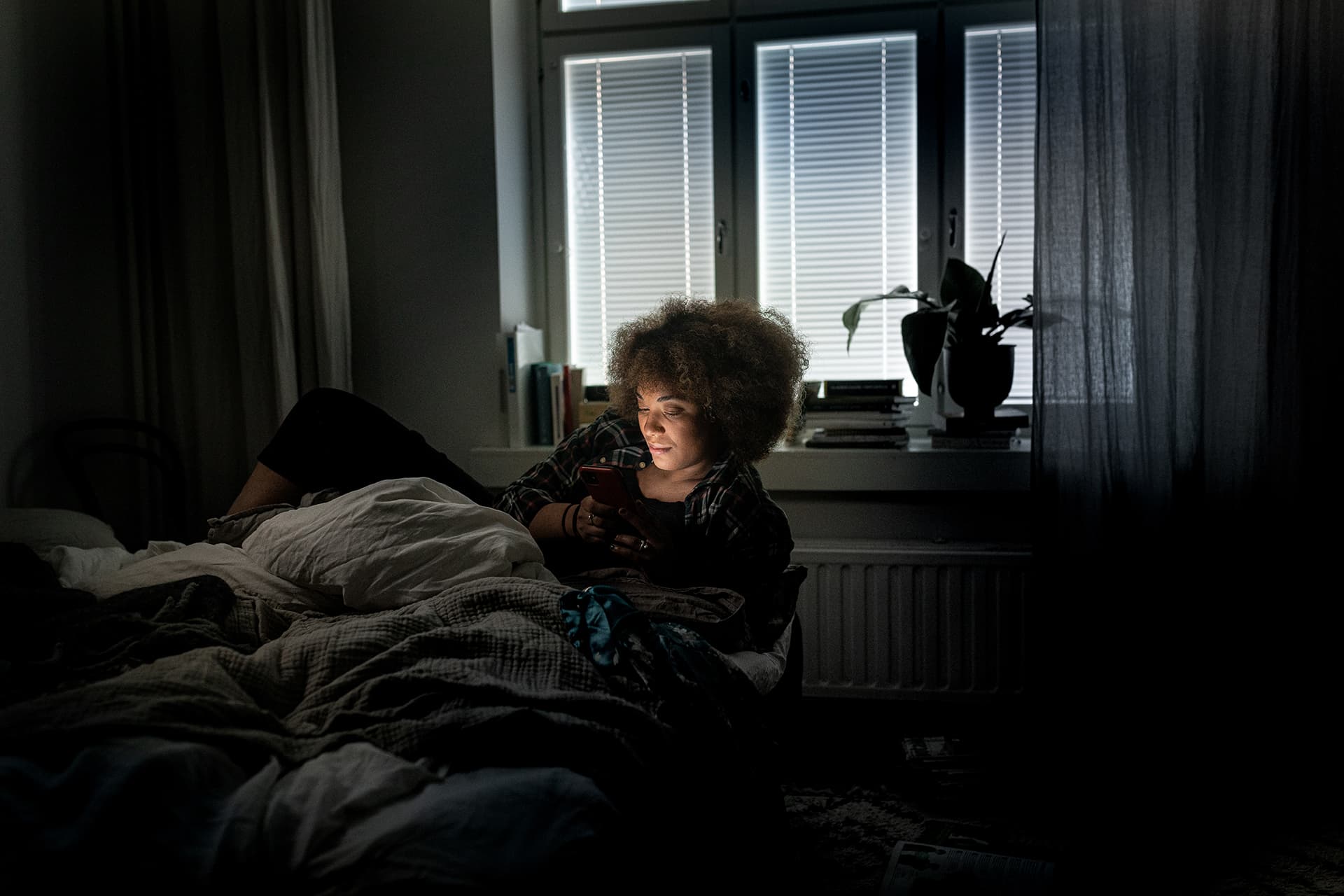 En ung kvinna surfar i sin telefon i sängen mitt i natten.