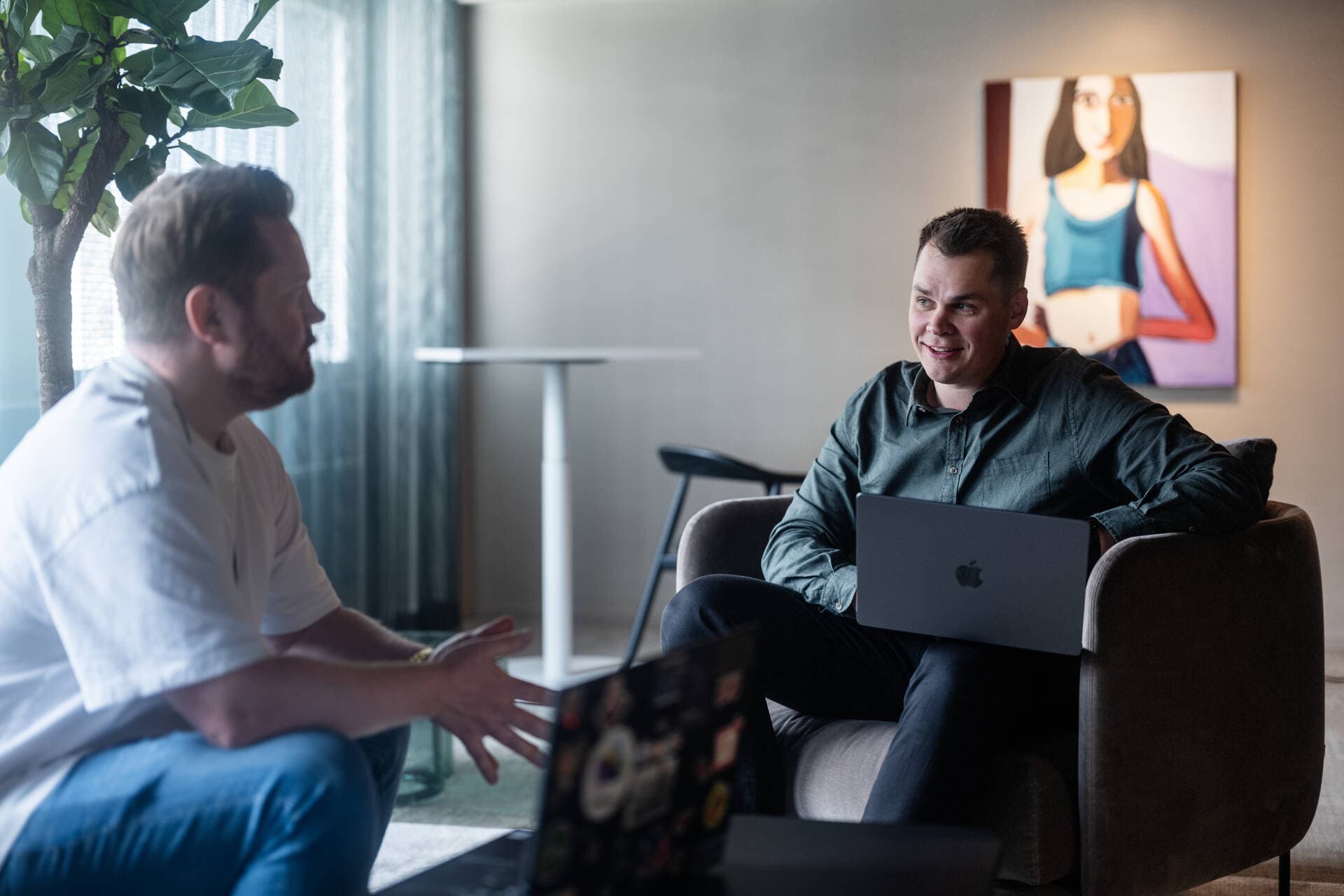 Kaksi digitaalisten palveluiden työntekijää istuvat nojatuoleissa ja juttelevat toisilleen neuvotteluhuoneessa.