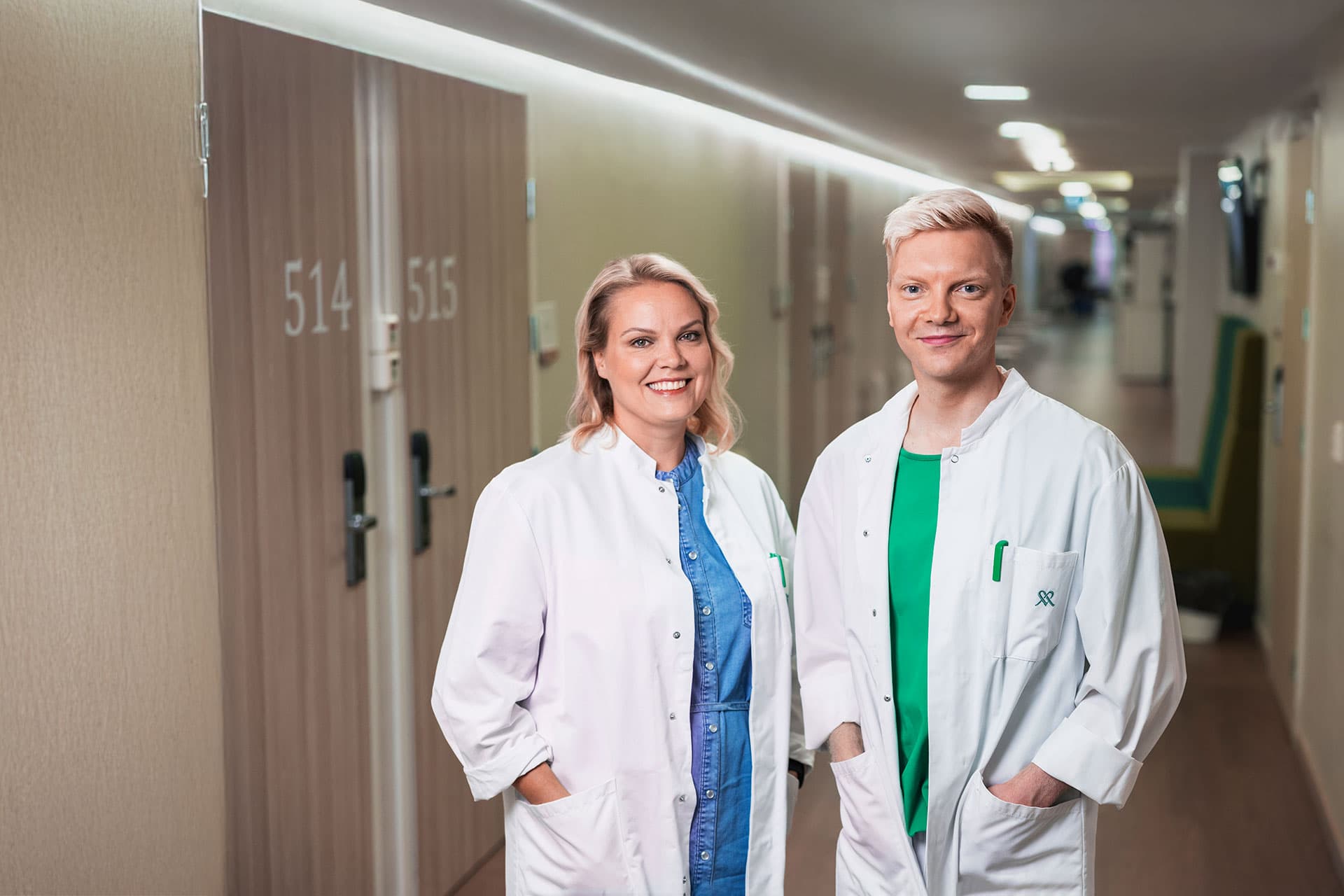 Mehiläisen lääkärit Hannele ja Niko seisovat iloisena lääkärikeskuksen käytävällä.
