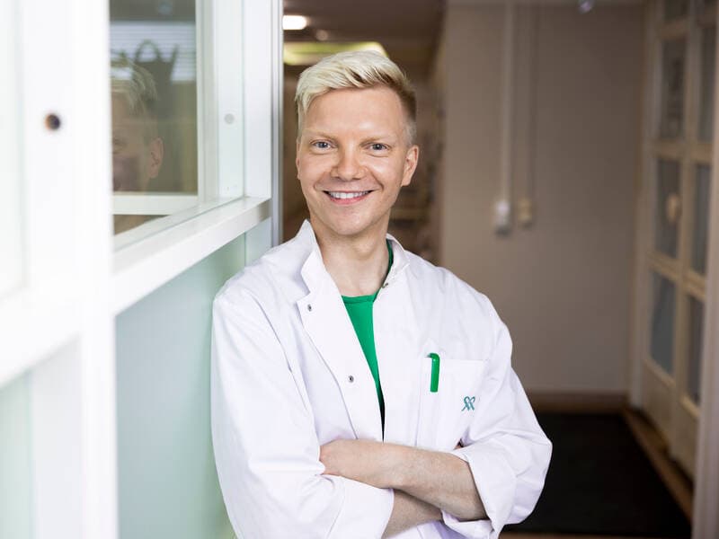 Mehiläisen lääkäri seisoo lääkärikeskuksen käytävällä ja poseeraa kameralle.
