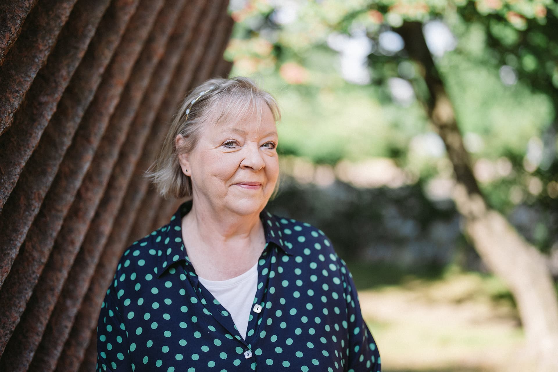 Kotipalvelu Mehiläisen henkilökohtainen avustaja Leena hymyilee puun varjossa.