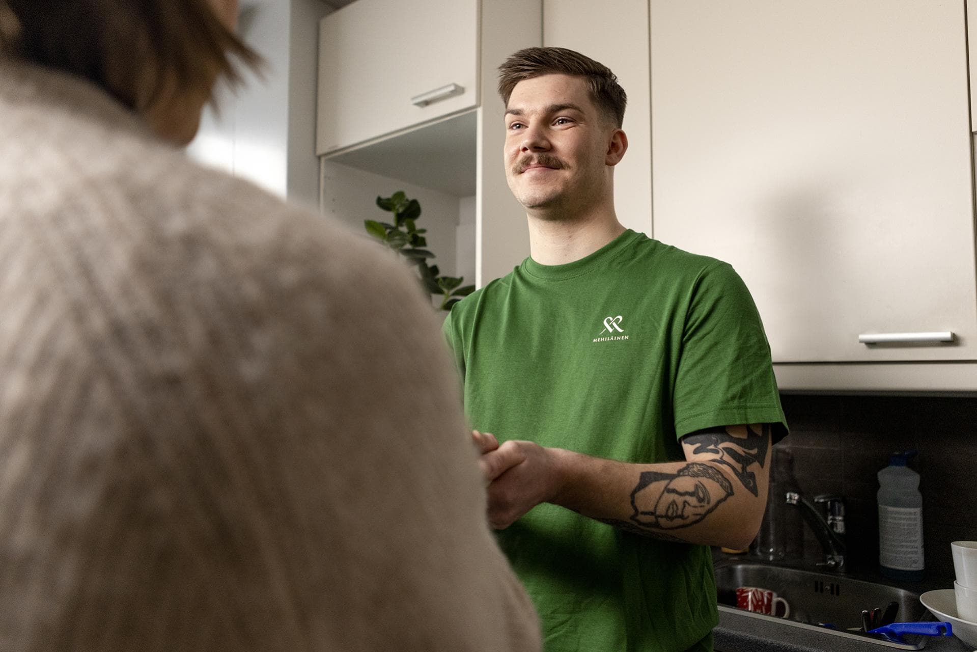 Mehiläinen Kotipalveluiden hoitaja kotisairaanhoitokäynnillä keskustelemassa asiakkaan keittiössä.