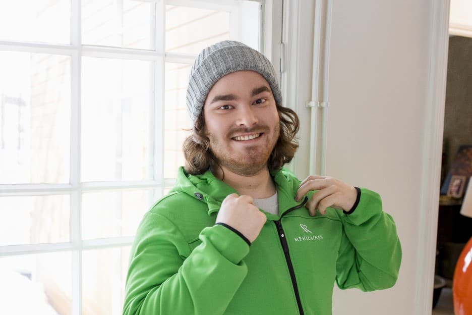 Henkiökohtainen avustaja hymyilee kameralle pukiessaan päälle Mehiläisen avustajan hupparia.