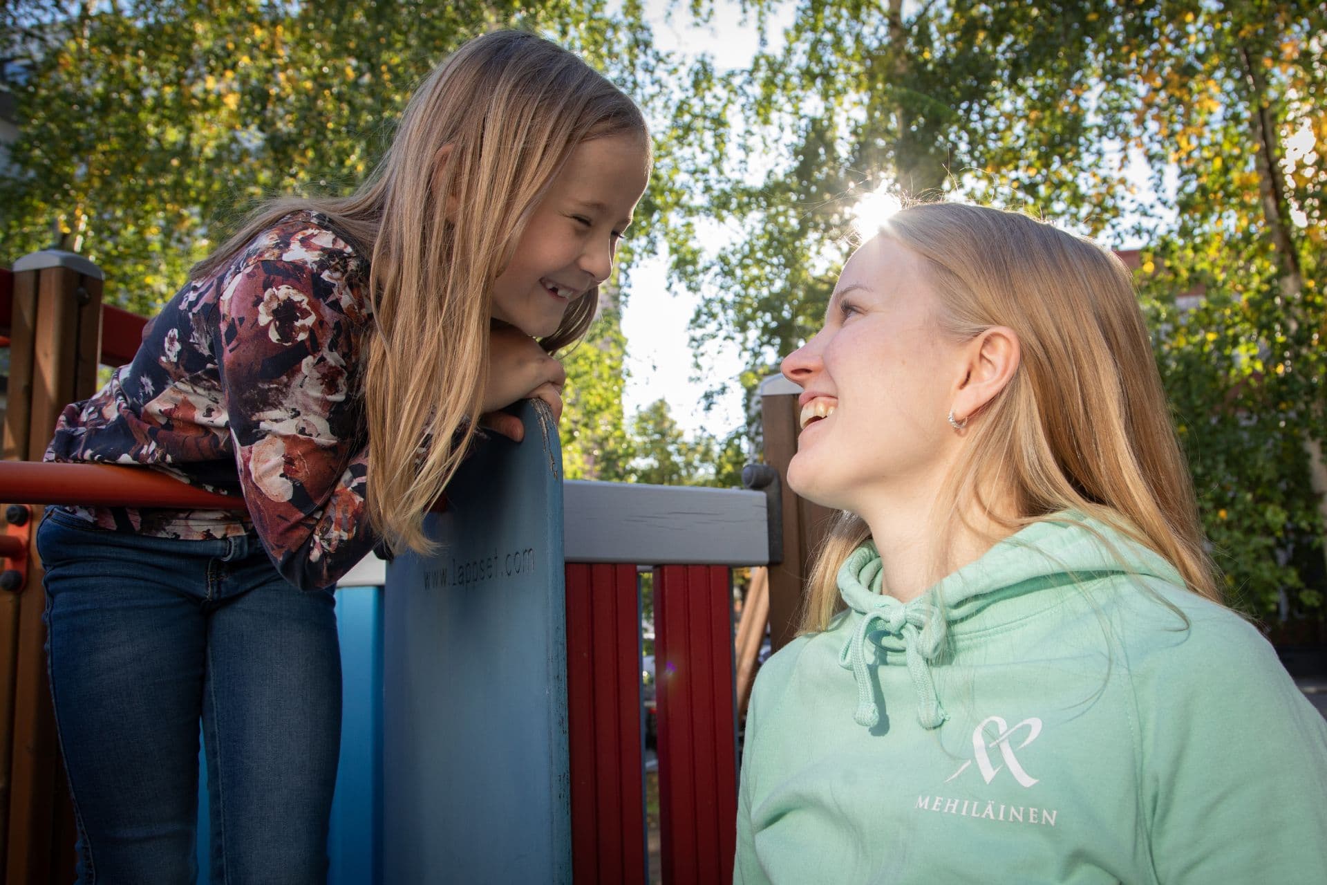 Toimintaterapeutti katsoo liukumäen huipulla leikkivää lasta silmiin nauraen.