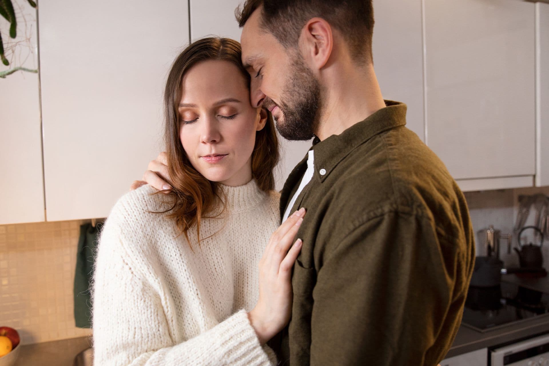 Lähikuva pariskunnasta keittiössä. Mies halaa naista ja heidän päänsä ovat vastakkain, molempien silmät ovat kiinni. Nainen pitelee miehen kättä.