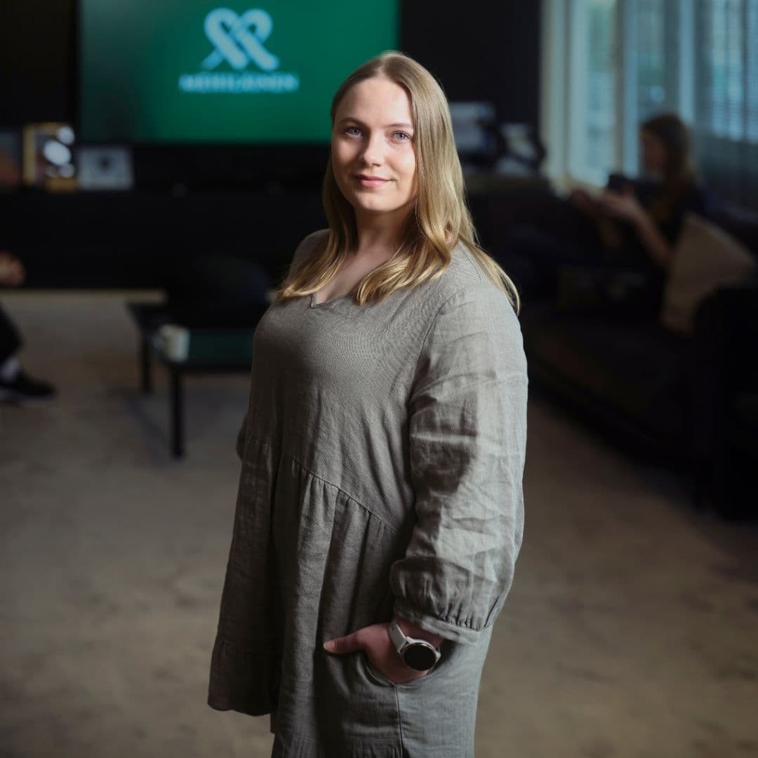 AI Ambassadorina toimiva Jenny seisoo käsi taskussa kameraan katsoen hämärässä toimistoympäristössä.