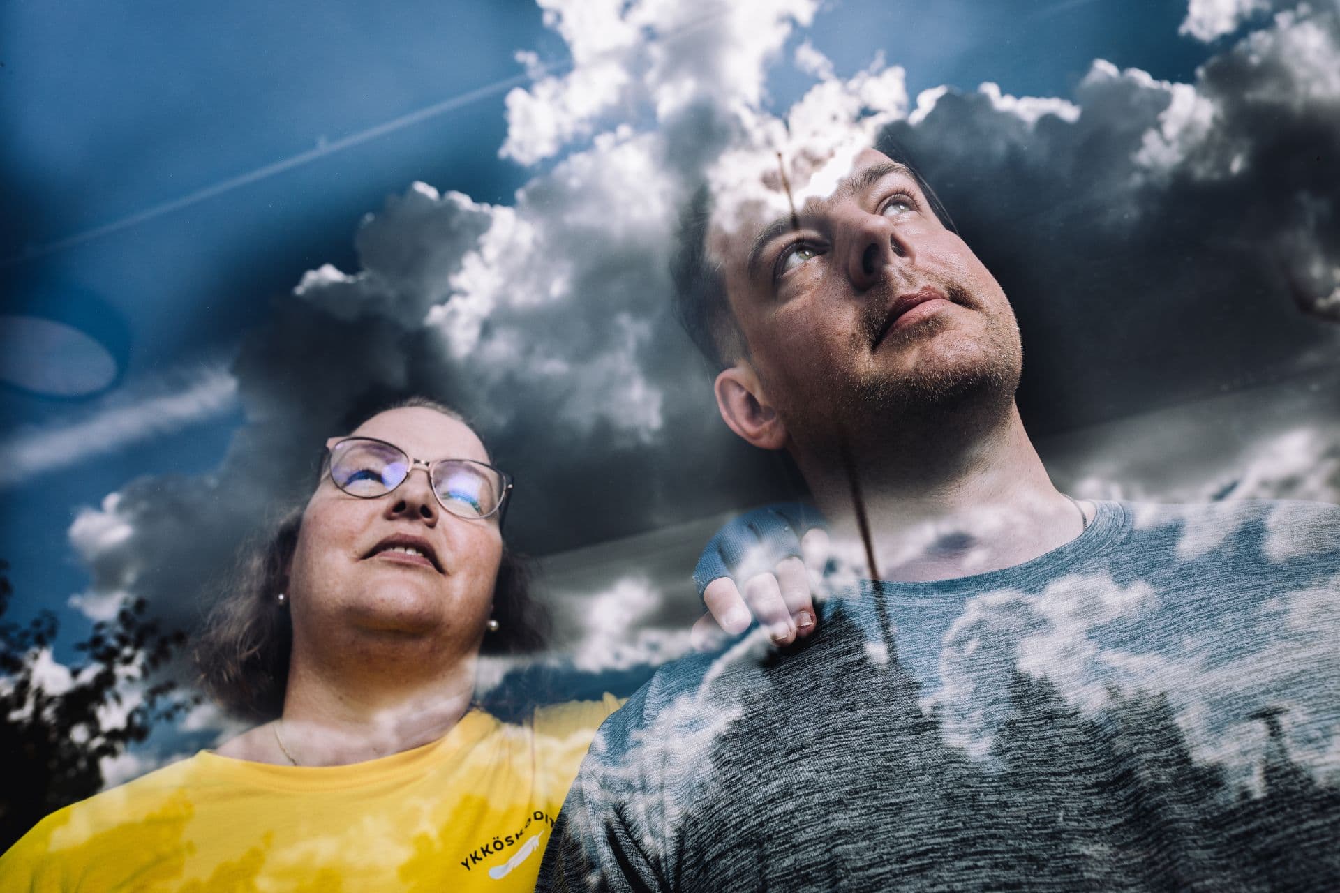 Kaksi ihmistä, mies ja nainen, katsovat ylöspäin. Heidän ylleen heijastuu ikkunasta pilviä ja sinistä taivasta, mikä symboloi toivoa ja ajatuksia masennuksen hoidosta.