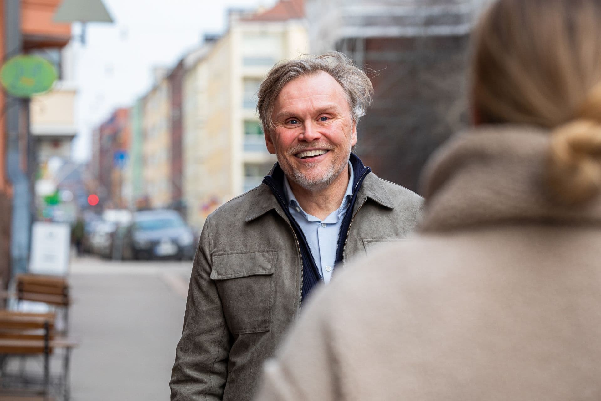 Hymyilevä keski-ikäinen mies katsoo vastaan kävelevää naista kaupunkiympäristössä.