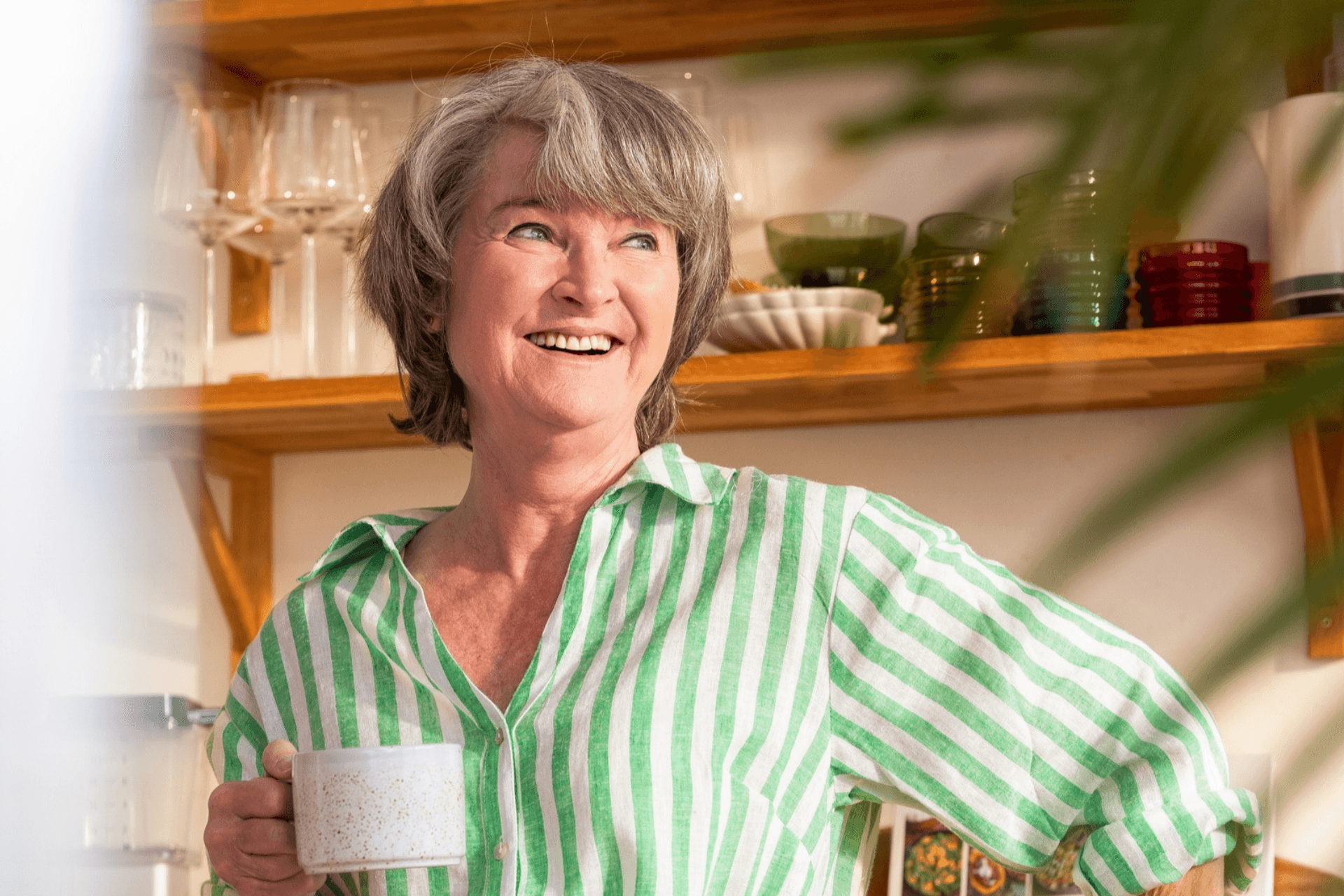 Woman smiles in her home holding a cup in her hand.