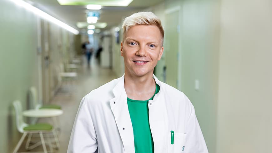 Mehiläisen yleislääkäri Niko hymyilee iloisesti lääkärikeskuksen käytävällä.