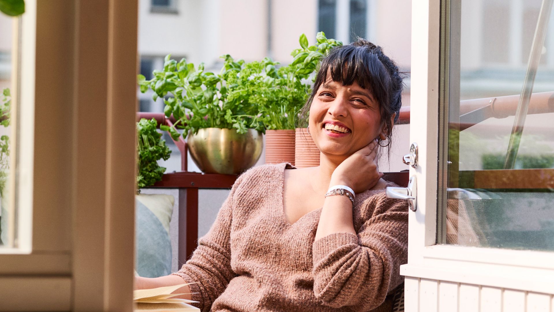 Nainen istuu parvekkeella ja katsoo hymyillen kameraan