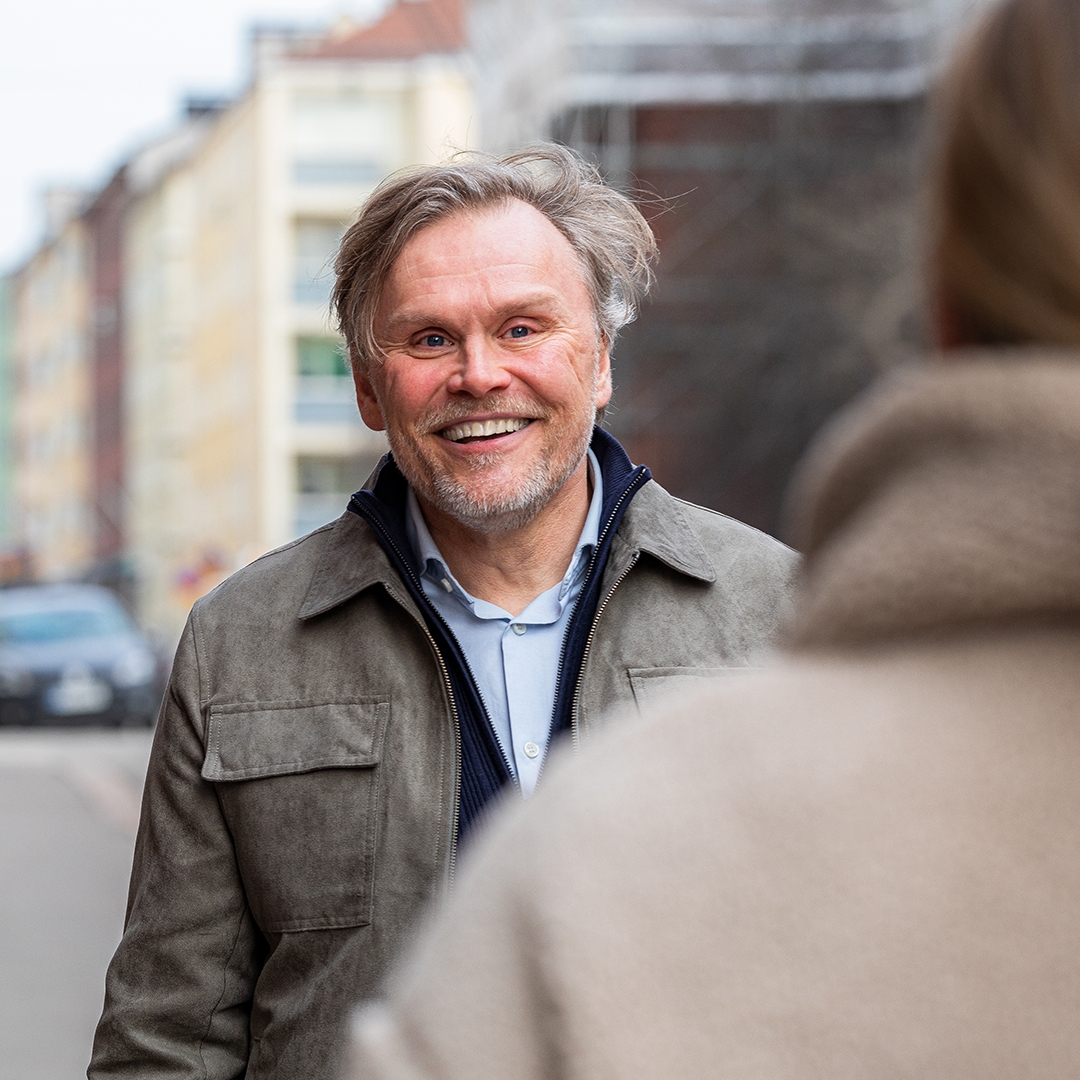 Keski-ikäinen mies hymyilee iloisesti kohdatessaan kadulla tutun vastaantulijan.