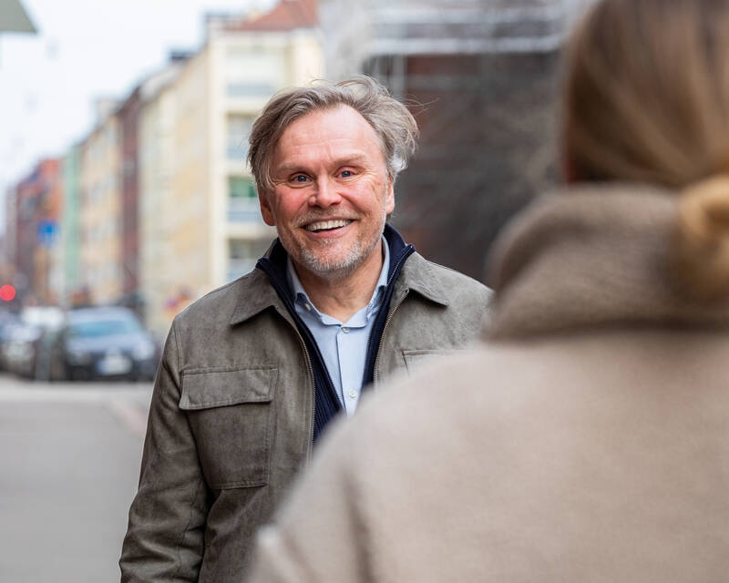Iäkkäämpi mies hymyilee kadulla tutulle vastaantulijalle.