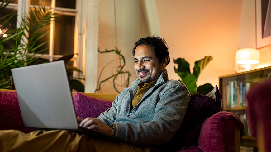 Keski-ikäinen mies istuu kotisohvalla läppäri sylissä ja asioi Digiklinikalla.