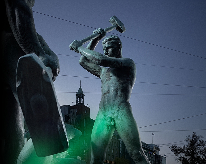 Vihreällä valolla valaistu Kolmen sepän patsas.