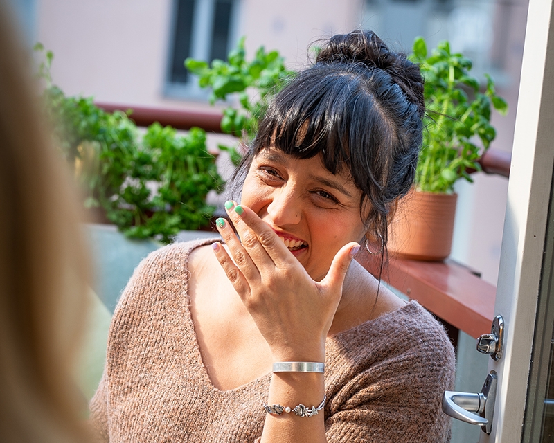 Nainen nauraa parvekkeella auringonpaisteessa.