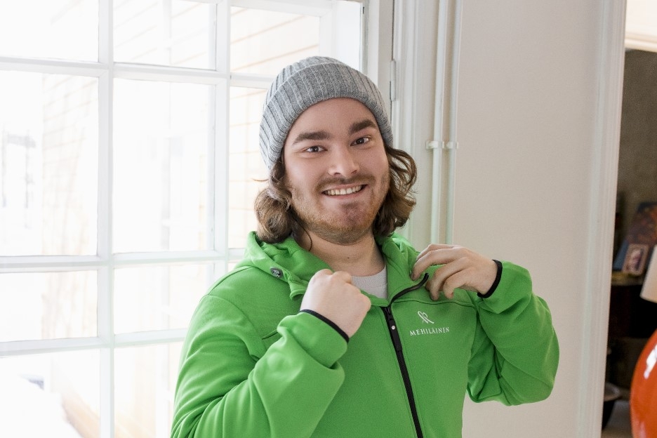 Henkiökohtainen avustaja hymyilee kameralle pukiessaan päälle Mehiläisen avustajan hupparia.