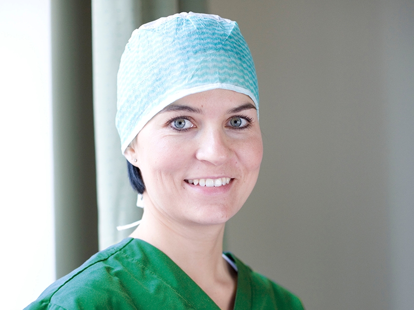 Mehiläisen leikkaussairaanhoitaja hymyilee leikkausvaatteet päällään leikkauksen jälkeen.